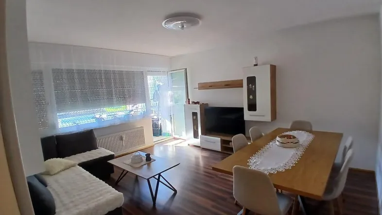 Heller Wohn- und Essbereich mit Holzboden, modernem Mobiliar und Zugang zum Balkon.