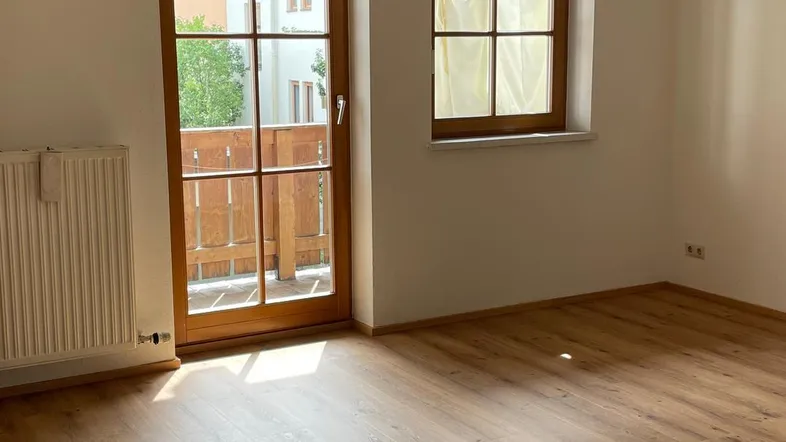 Helles Zimmer mit Laminatboden, weiß gestrichenen Wänden und Zugang zu einem Balkon.