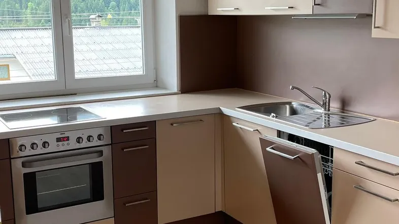 Moderne Küche mit Einbaugeräten, Holzdecke und Blick auf die grüne Landschaft und Berge.