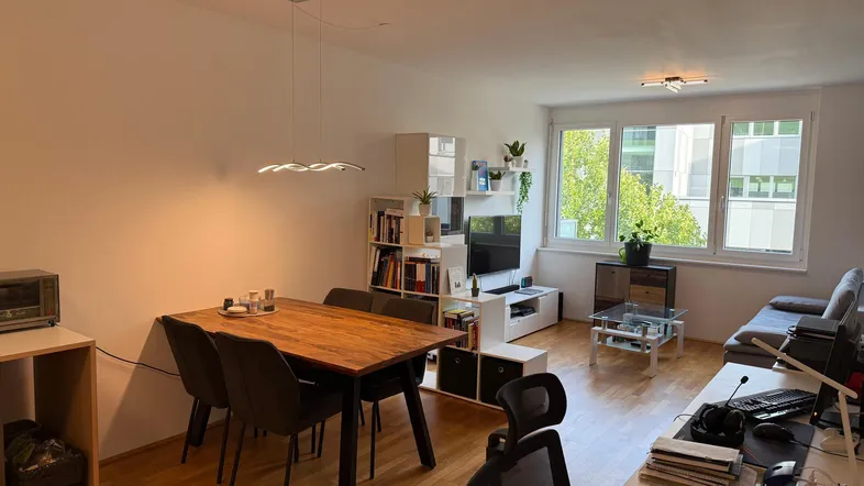 Heller offener Wohn- und Essbereich mit Holzboden, modernem Esstisch und Arbeitsplatz am Fenster.