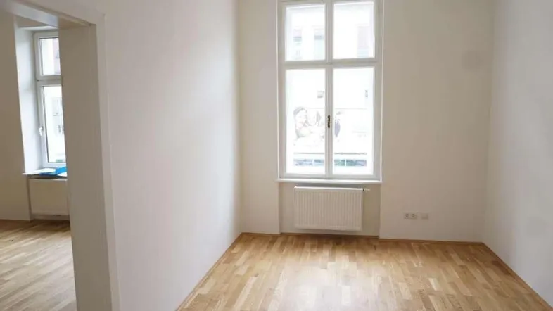 Heller, unmöblierter Raum mit Parkettboden und großem Fenster, bereit zur individuellen Gestaltung.