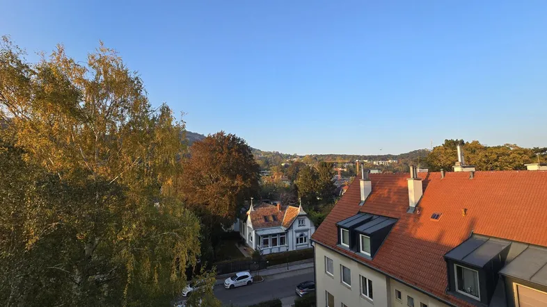 Weitblick über Dächer, Bäume und die umliegende Hügellandschaft an einem sonnigen Tag.