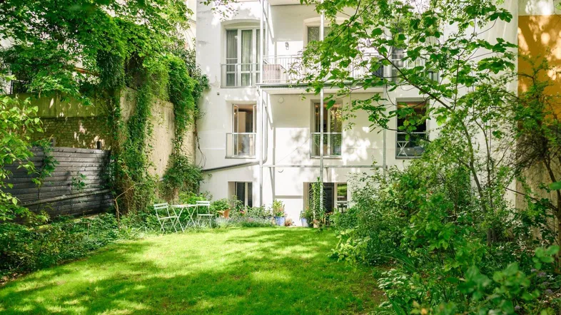 Grüner Gartenbereich mit Rasenfläche und kleiner Sitzgruppe vor der hellen Gebäudefassade.