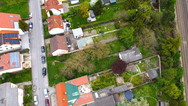 Luftaufnahme eines Wohngebiets mit mehreren Grundstücken, Häusern und angrenzenden Bahngleisen.