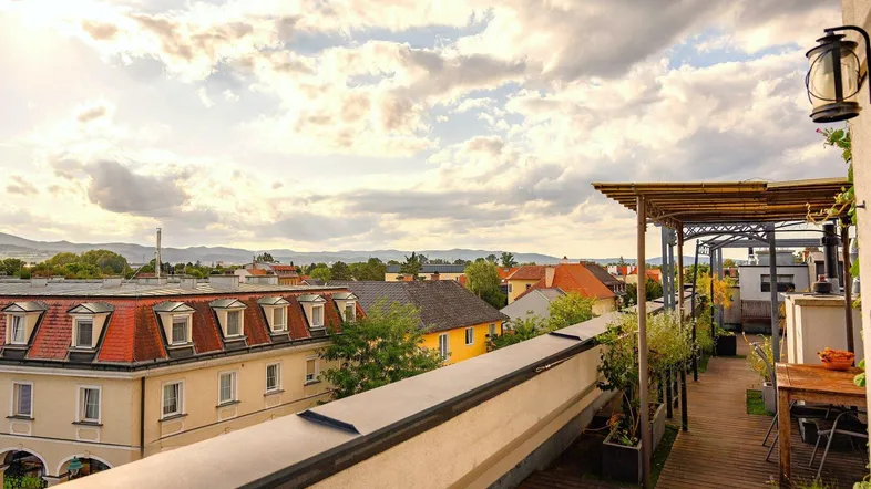 Dachterrasse mit Holzboden, Sitzbereich und weitem Blick über die Stadt und Berge.