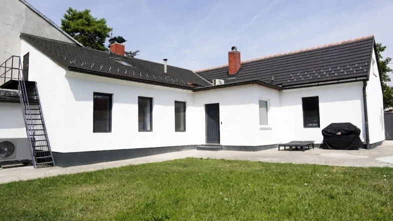 Weißes Haus mit dunklem Dach und grünem Rasen im Außenbereich.