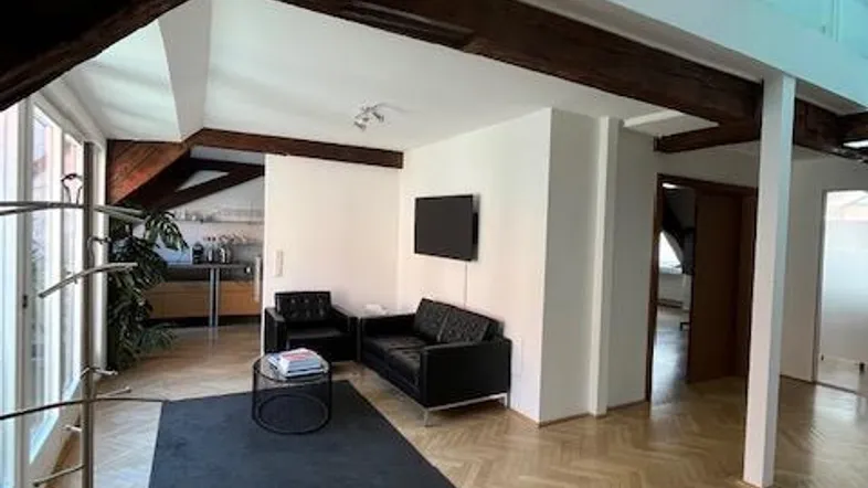 Geräumiges Wohnzimmer mit Holzbalken, Fischgrätparkett und einem modernen Glasdach, das viel Licht hereinlässt.