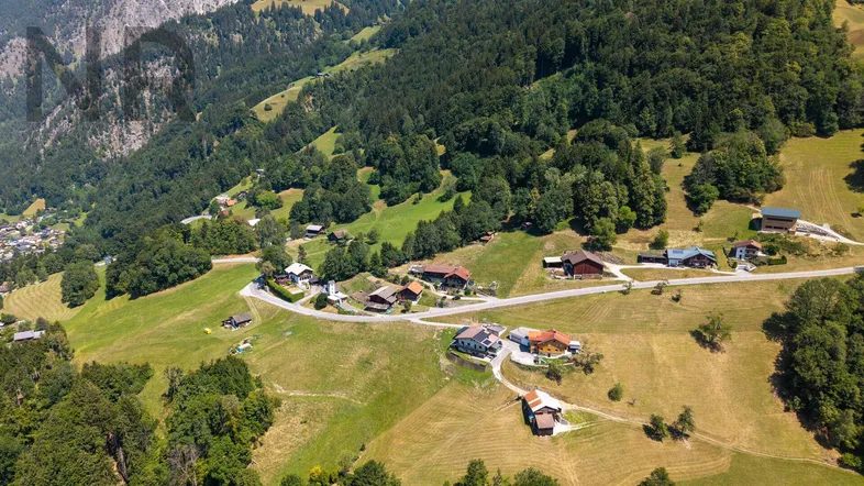 Luftaufnahme eines malerischen Dorfes in einem grünen Tal, umgeben von bewaldeten Bergen.