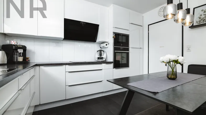 Moderne Einbauküche mit weißen Hochglanzfronten, dunkler Arbeitsplatte und Essbereich.