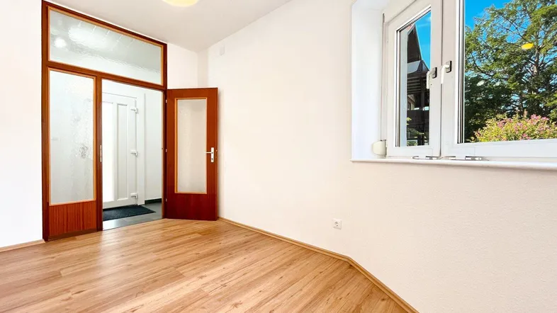 Helles Zimmer mit Laminatboden, großen Fenstern und Blick ins Grüne.