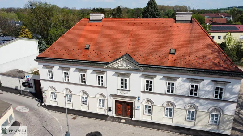 Historisches Gebäude mit weißer Fassade, rotem Ziegeldach und vielen Fenstern in einer ländlichen Umgebung.