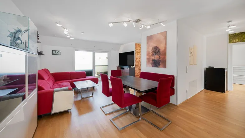 Geräumiger Wohn-Essbereich mit rotem Sofa, Esstisch und Zugang zu einem Balkon.