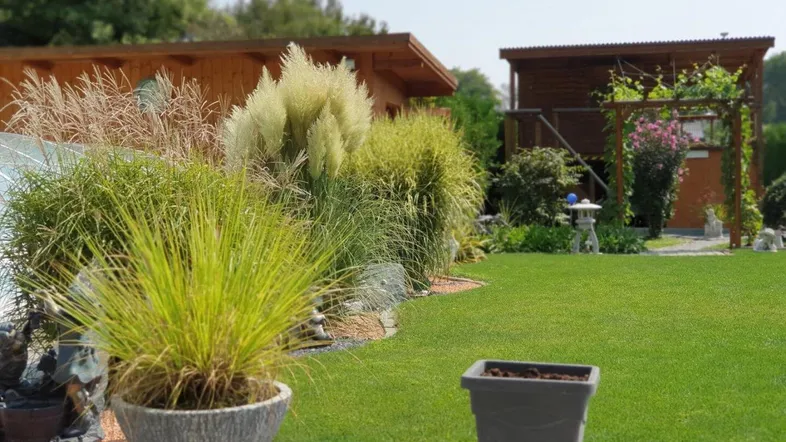 Gepflegter Gartenbereich mit üppiger Bepflanzung und einem Gartenhaus im Hintergrund unter blauem Himmel.