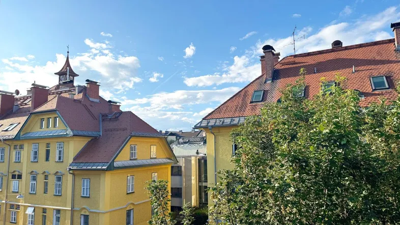 Blick auf traditionelle Gebäude mit roten Ziegeldächern und grünen Bäumen unter blauem Himmel.