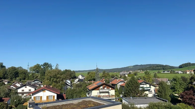 Weitblick über Dächer und grüne Hügel unter strahlend blauem Himmel an einem sonnigen Tag.