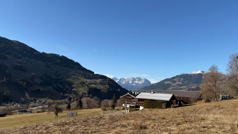 Weitläufige Landschaft mit Bergen im Hintergrund und einem traditionellen Gebäude im Tal unter blauem Himmel.