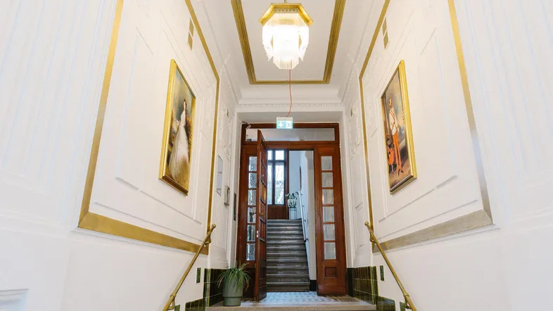Elegantes Treppenhaus mit Stuckverzierungen, goldenen Akzenten und klassischer Beleuchtung.