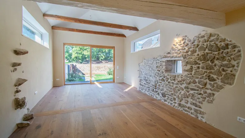 Geräumiger Wohnbereich mit Holzdielenboden, freiliegenden Steinwänden und großen Fenstern zum Garten.