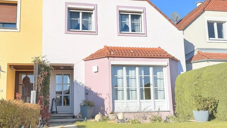 Vorderansicht eines Reihenhauses mit gepflegtem Vorgarten und heller Fassade unter blauem Himmel.