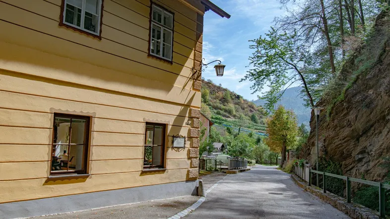 Gelbe Hausfassade an einer Straße mit Blick auf bewaldete Hügel und Berge.