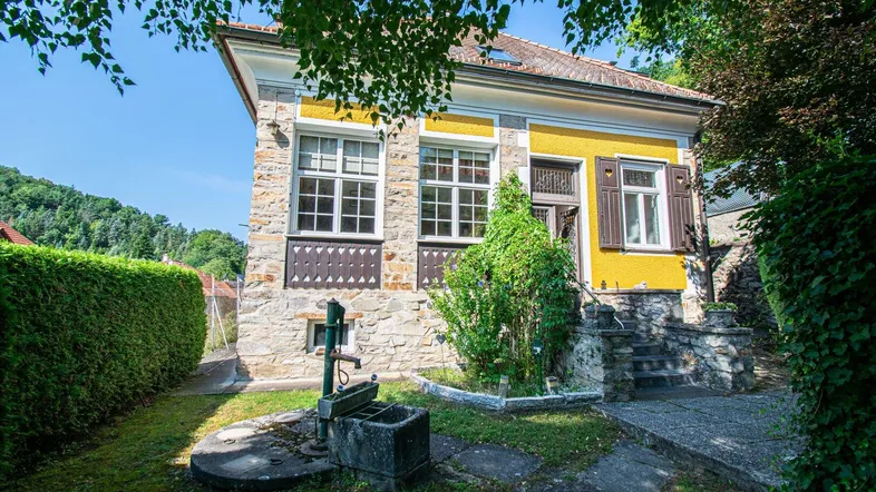 Historisches Haus mit gelber Fassade, Steinelementen und einem charmanten Vorgarten mit alter Wasserpumpe.