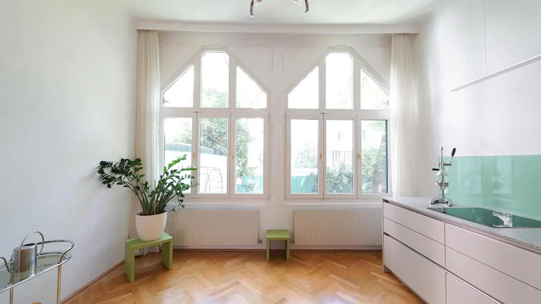 Helle Küche mit moderner Arbeitsplatte, Spüle und großen Fenstern mit Blick ins Grüne.