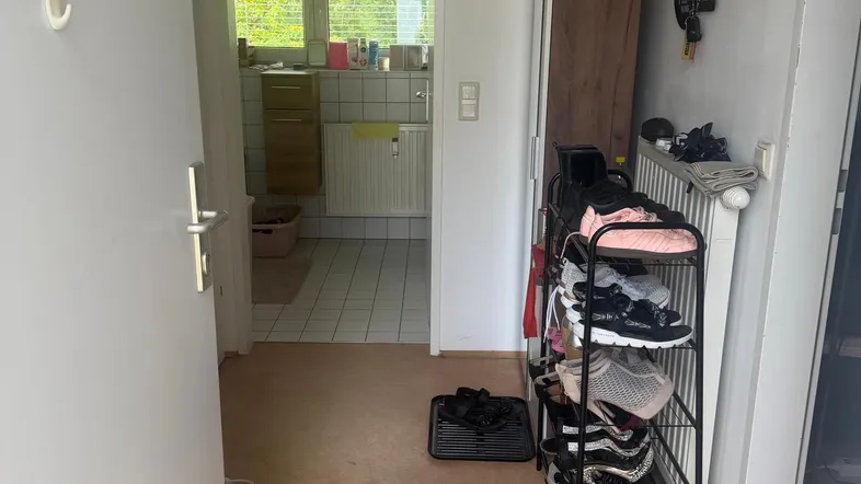 Eingangsbereich mit Korkboden, Schuhregal und Blick in ein gefliestes Badezimmer.
