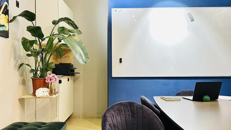 Moderner Büroraum mit blauer Akzentwand, Whiteboard und bequemen Sitzgelegenheiten für Besprechungen.