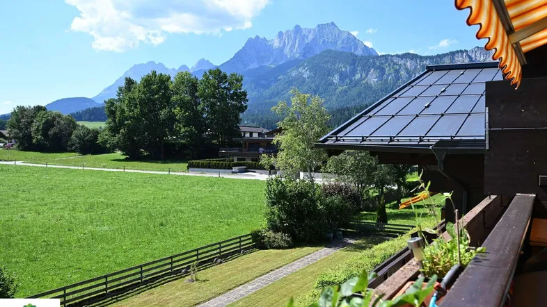 Geräumiger Balkon mit Markise, Bergblick und Blick auf grüne Wiesen unter blauem Himmel.