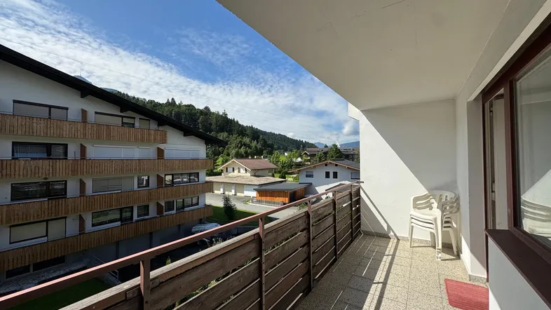 Geräumiger Balkon mit Holzzaun und weitem Blick auf die umliegende Berglandschaft und das Dorf.