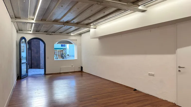 Geräumiger Innenraum mit Holzbalkendecke, Holzboden und einem großen Fenster, das Tageslicht hereinlässt.