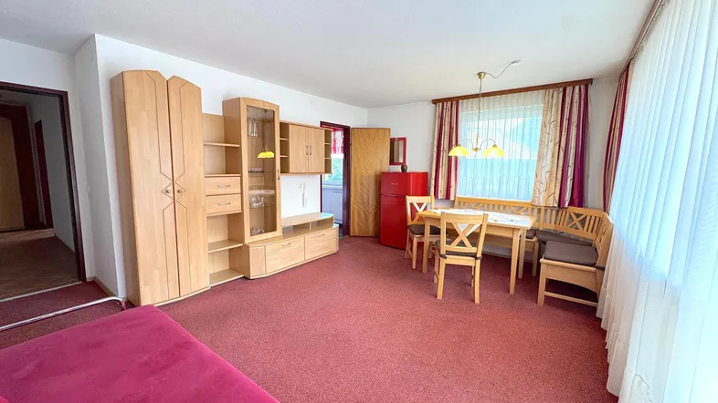 Gemütlicher Wohn- und Essbereich mit Teppichboden, Holzmöbeln und einem roten Kühlschrank.