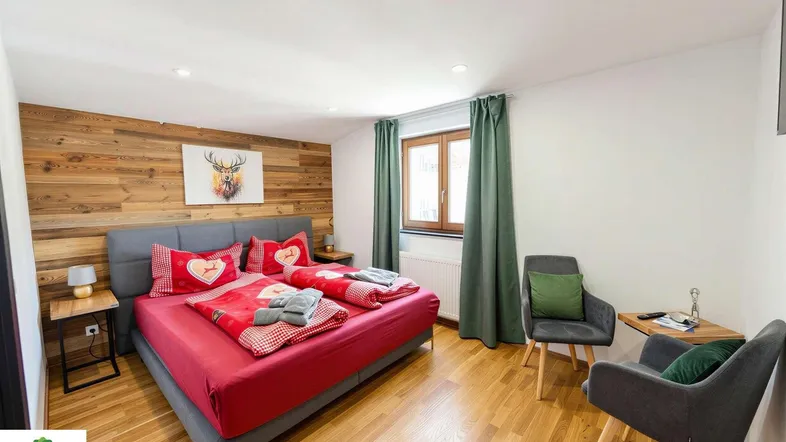 Gemütliches Schlafzimmer mit Holzwand, großem Bett und bequemen Sesseln, hell und modern eingerichtet.