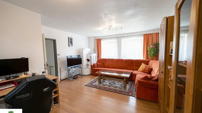 Helles Wohnzimmer mit orangefarbenem Ecksofa, Holzboden und Arbeitsbereich.