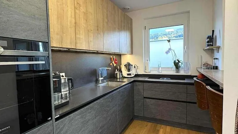 Moderne Küche mit grauen Fronten, Holzakzenten und einem Fenster mit Seeblick.