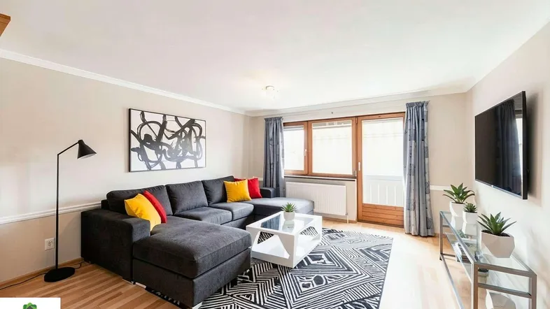 Gemütliches Wohnzimmer mit großem Ecksofa, Holzboden und Zugang zu einem Balkon oder Terrasse.
