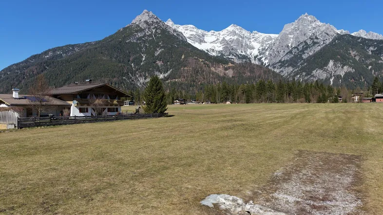 Weitläufiges Feld mit traditionellen Häusern und majestätischem Alpenpanorama im Hintergrund.