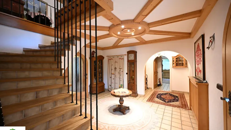 Traditioneller Eingangsbereich mit Holztreppe, Fliesenboden und dekorativer Holzdecke.