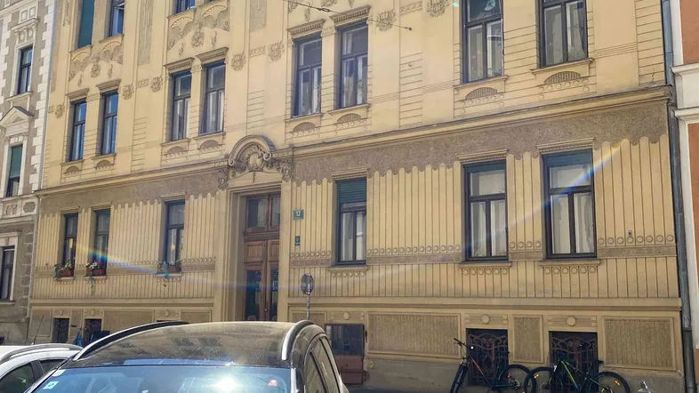 Historisches Gebäude mit reich verzierter Fassade und parkenden Autos davor in der Stadt.