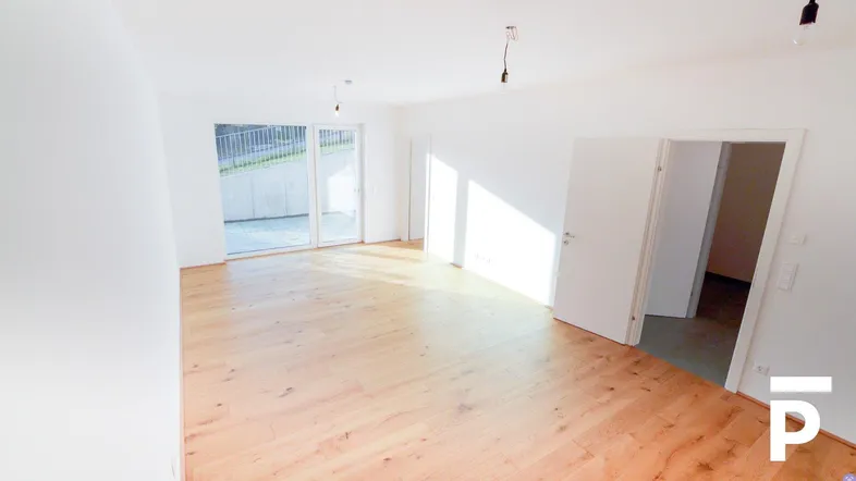 Helles, leeres Zimmer mit Holzboden und Zugang zu einem Außenbereich, ideal als Wohnzimmer.