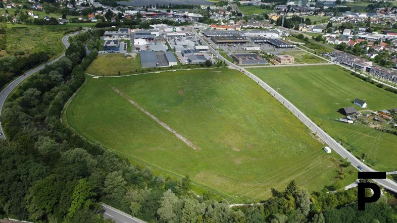 Luftaufnahme eines großen grünen Feldes mit umliegenden Straßen und Bebauung in der Ferne.