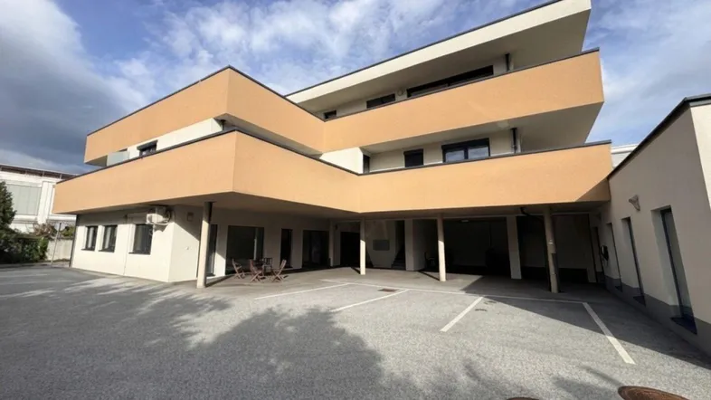Modernes Gebäude mit mehreren Etagen und einer hellbraunen Fassade unter bewölktem Himmel.