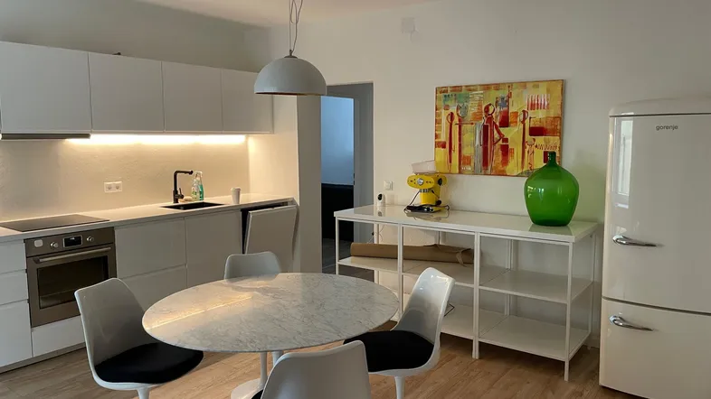 Moderne Küche mit weißen Hochglanzfronten, Esstisch und hellem Holzfußboden.