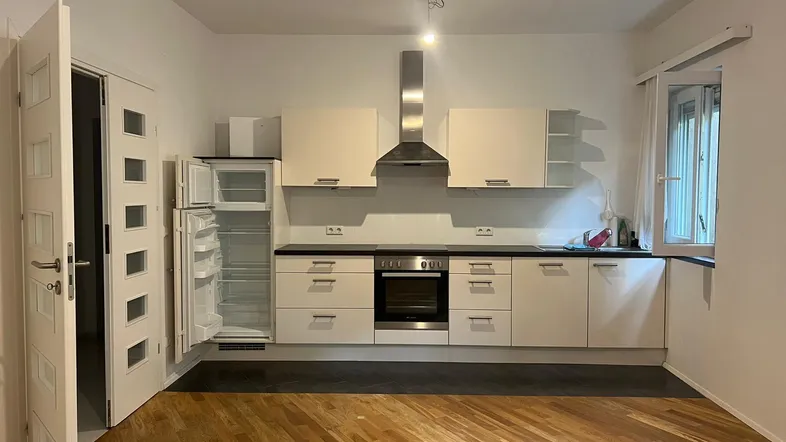 Moderne Einbauküche mit hellen Schränken, Edelstahlgeräten und Holzboden in einem offenen Raum.