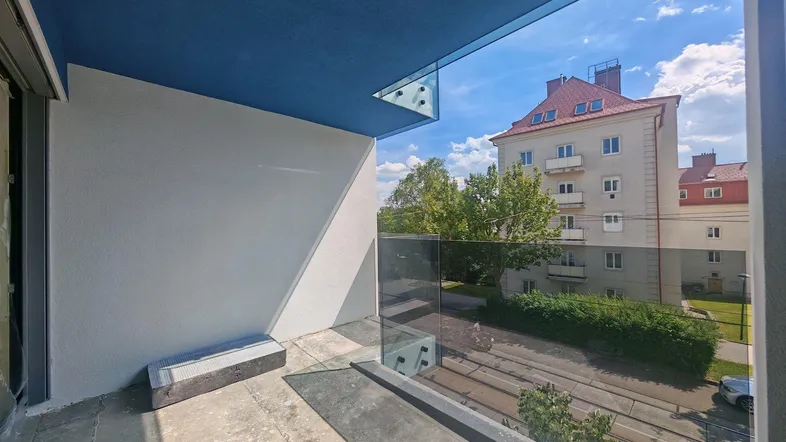 Balkon im Rohbau mit Glasgeländer und blauer Decke, bietet Stadtblick.