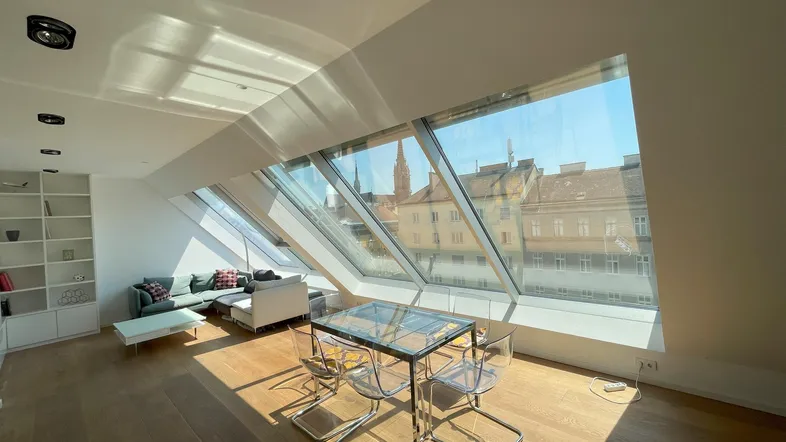 Helles Wohn- und Esszimmer mit großen Dachfenstern, Holzboden und Blick auf die Stadt.