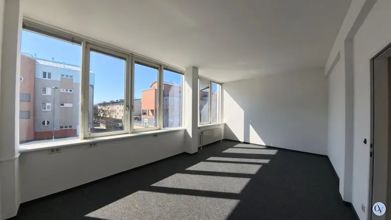 Heller Büroraum mit großen Fenstern, die viel Tageslicht hereinlassen und einen Blick auf umliegende Gebäude bieten.