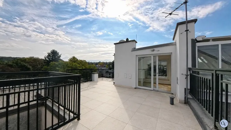 Große Dachterrasse mit Fliesenboden und Blick auf die Umgebung unter blauem Himmel.