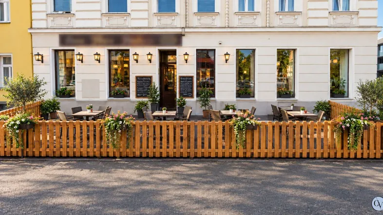 Gemütliche Außenterrasse eines Restaurants mit Holzzaun und Blumenkästen vor einem Gebäude.