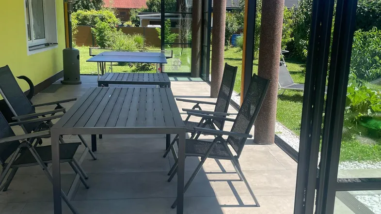 Überdachte Terrasse mit Glasfronten und Esstischen, perfekt für Mahlzeiten im Freien bei jedem Wetter.